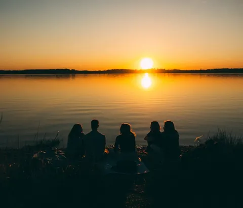 Friends silhouetted against a lake at sunset.